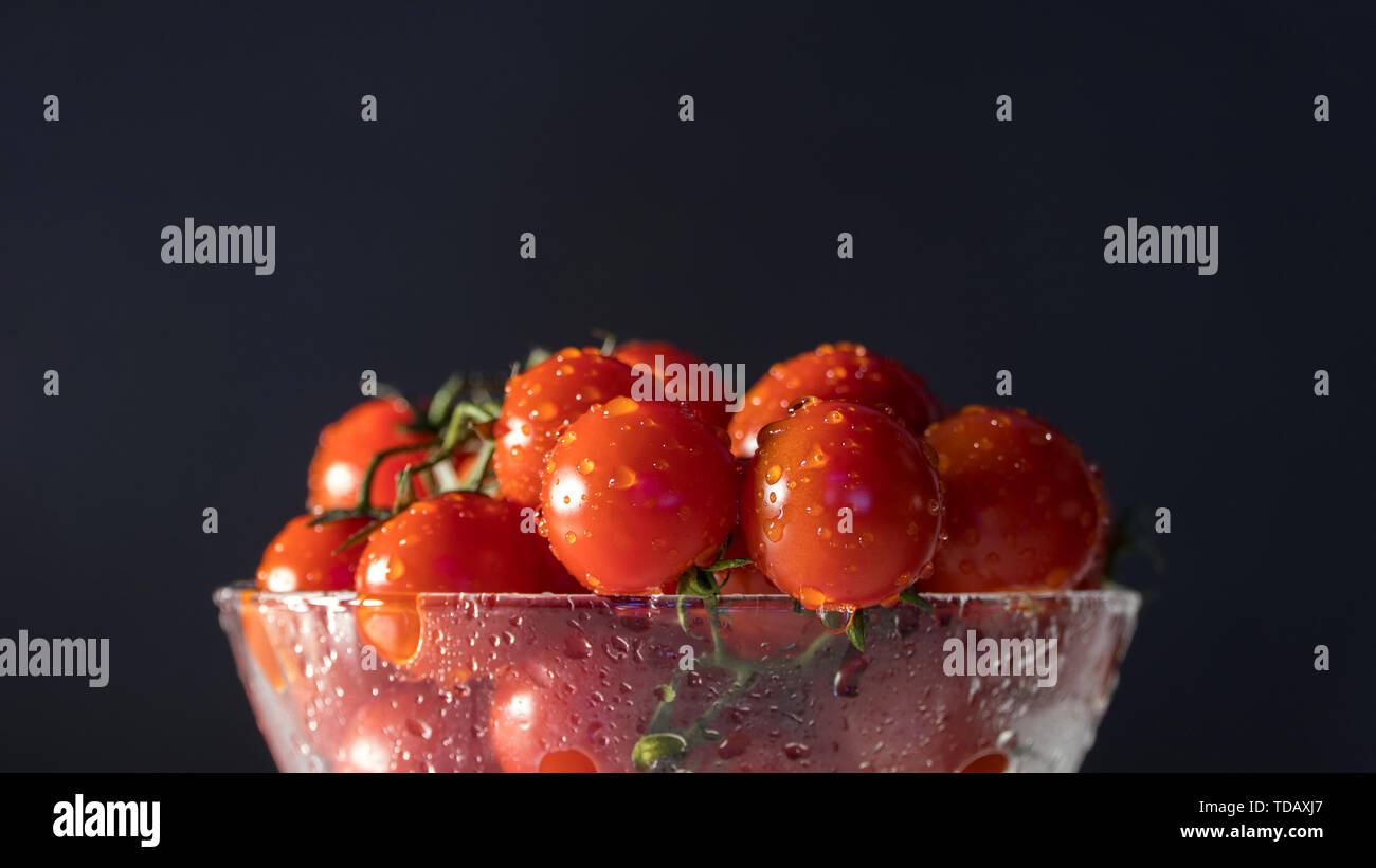 tomatoes with water drops in a glass bowl on a black background, directional lighting. horizontal plane Stock Photo