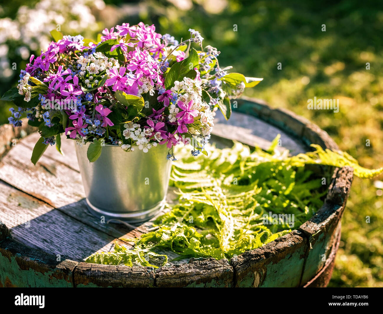 Bouquet of flowers in tin pots on an old wooden barrel. Wedding outdoor floristics Stock Photo