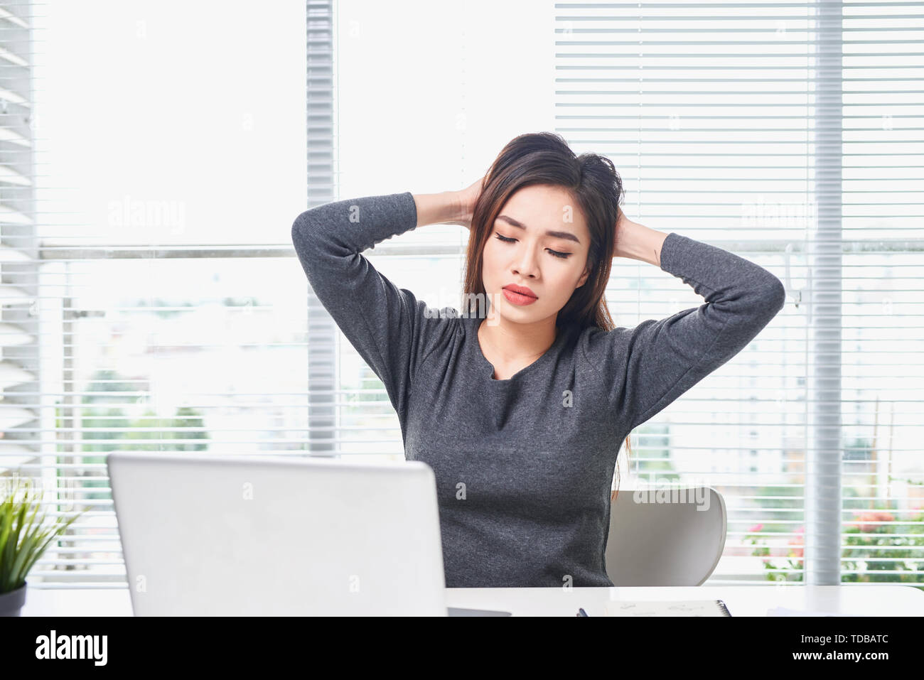 Young bored woman feeling drowsy at office sitting with laptop computer. Stock Photo