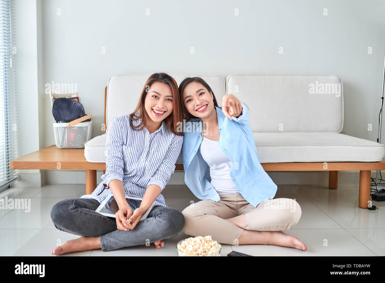 Wondered amazed impressed girl gesturing forefinger eating popcorn watching funny comic program with her friend sitting in living room indoor enjoying Stock Photo