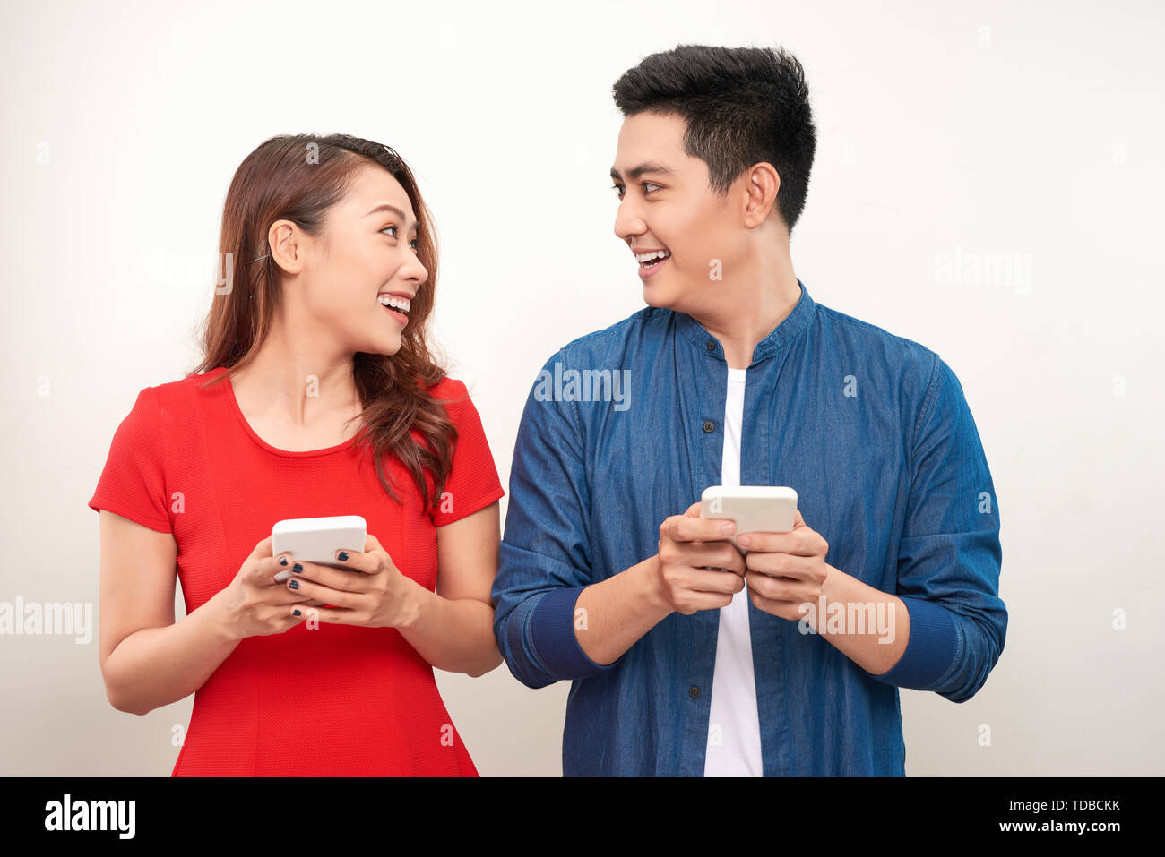 Beautiful smiling modern couple in casual wear with phones in hands on a white wall background Stock Photo