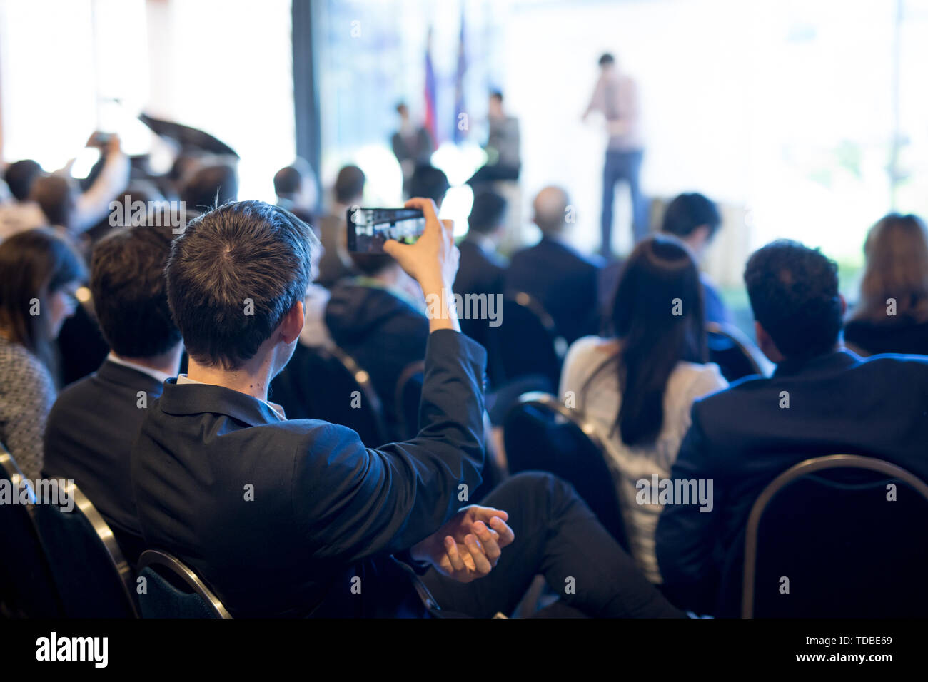 Businessman takes a picture of corporate business presentation at conference hall using smartphone. Stock Photo