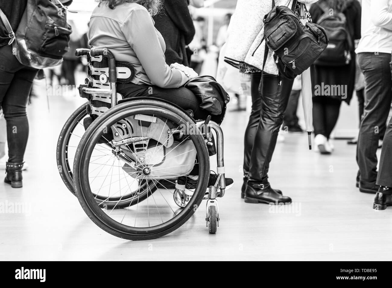 Close up of unrecognizable hanicapped woman on a wheelchair queuing in line to perform everyday tasks. Stock Photo