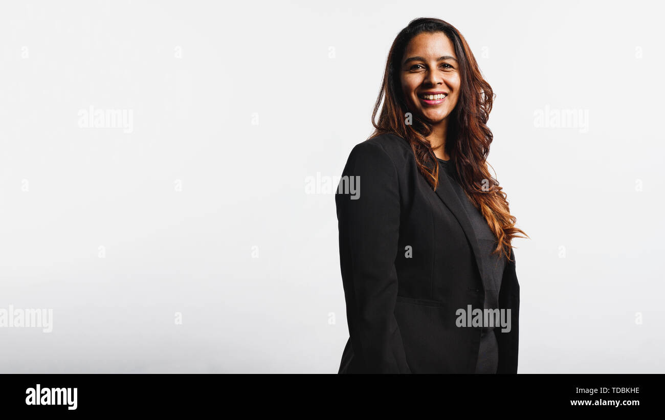 Side view of smiling businesswoman standing against white background looking at camera. Portrait of smiling businesswoman in formal suit having golden Stock Photo