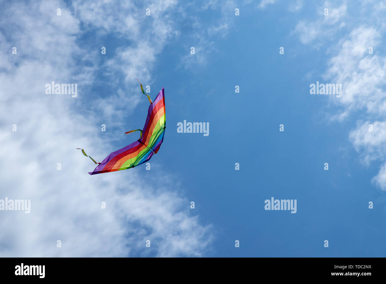 Multicolored kite on the background of the blue sky with clouds Stock Photo