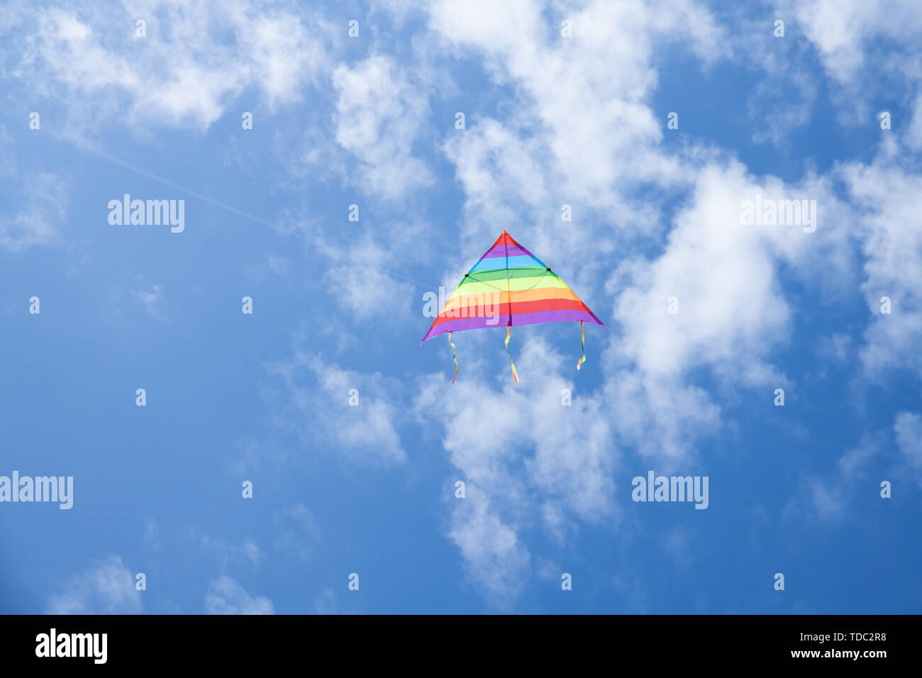 Multicolored kite on the background of the blue sky with clouds Stock Photo