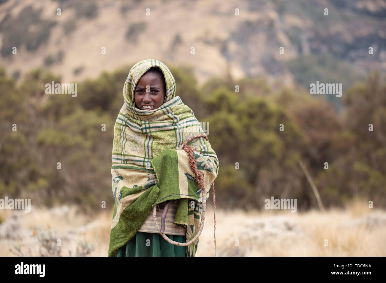 SIMIEN MOUNTAIN, ETHIOPIA, APRIL 25.2019, Little Ethiopian shepherdess girl veiled in a blanket with whip in cold morning. Simien Mountains, Ethiopia, Stock Photo