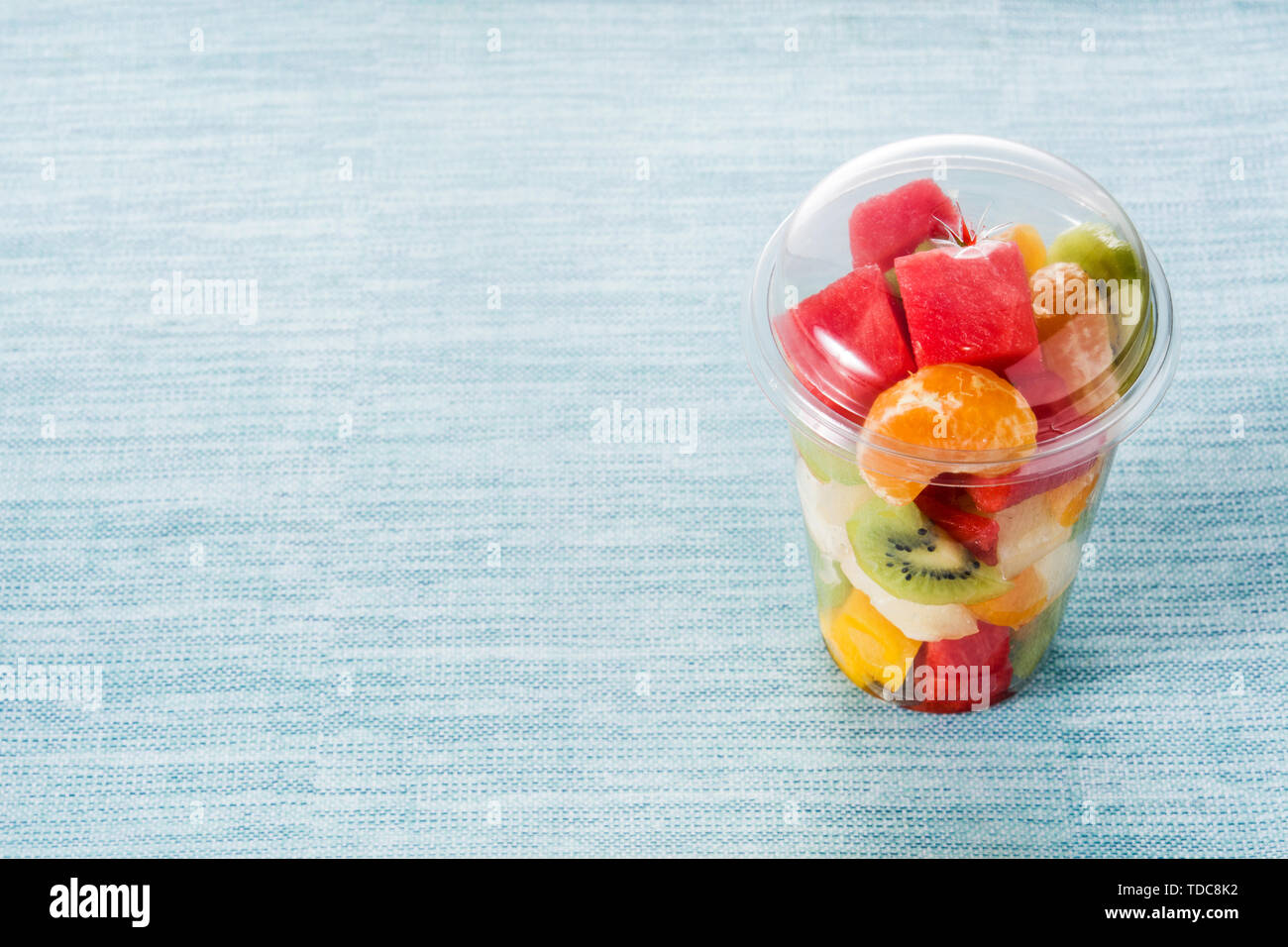 Fresh cut fruit in a plastic cup on blue background Stock Photo