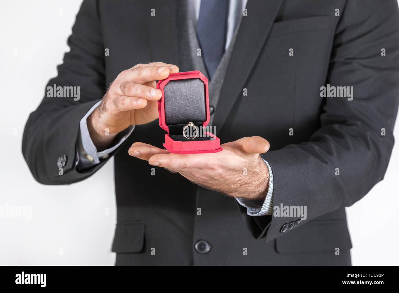 Man in a black suit gives a ring with a diamond in a red box Stock Photo