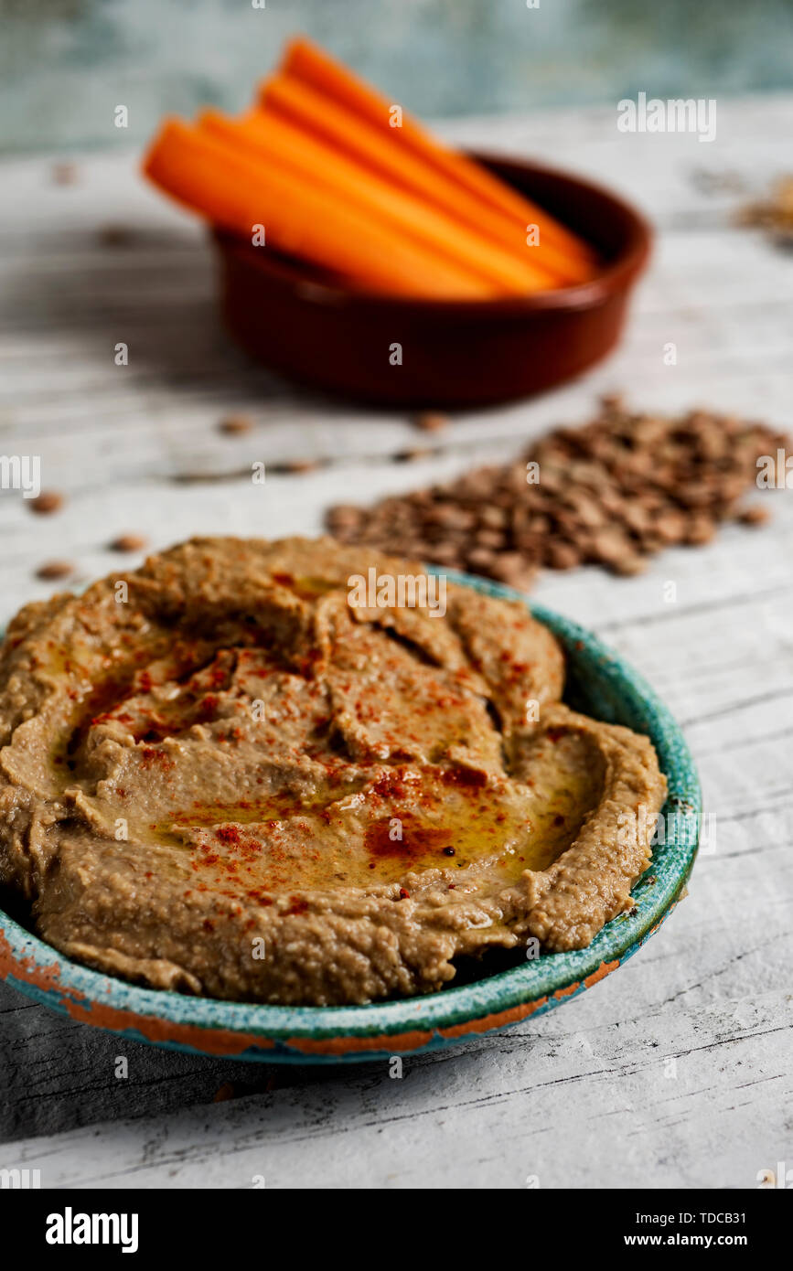 closeup of a homemade lentil hummus seasoned with paprika served in a green ceramic plate on a white rustic wooden table, and a bowl in the background Stock Photo