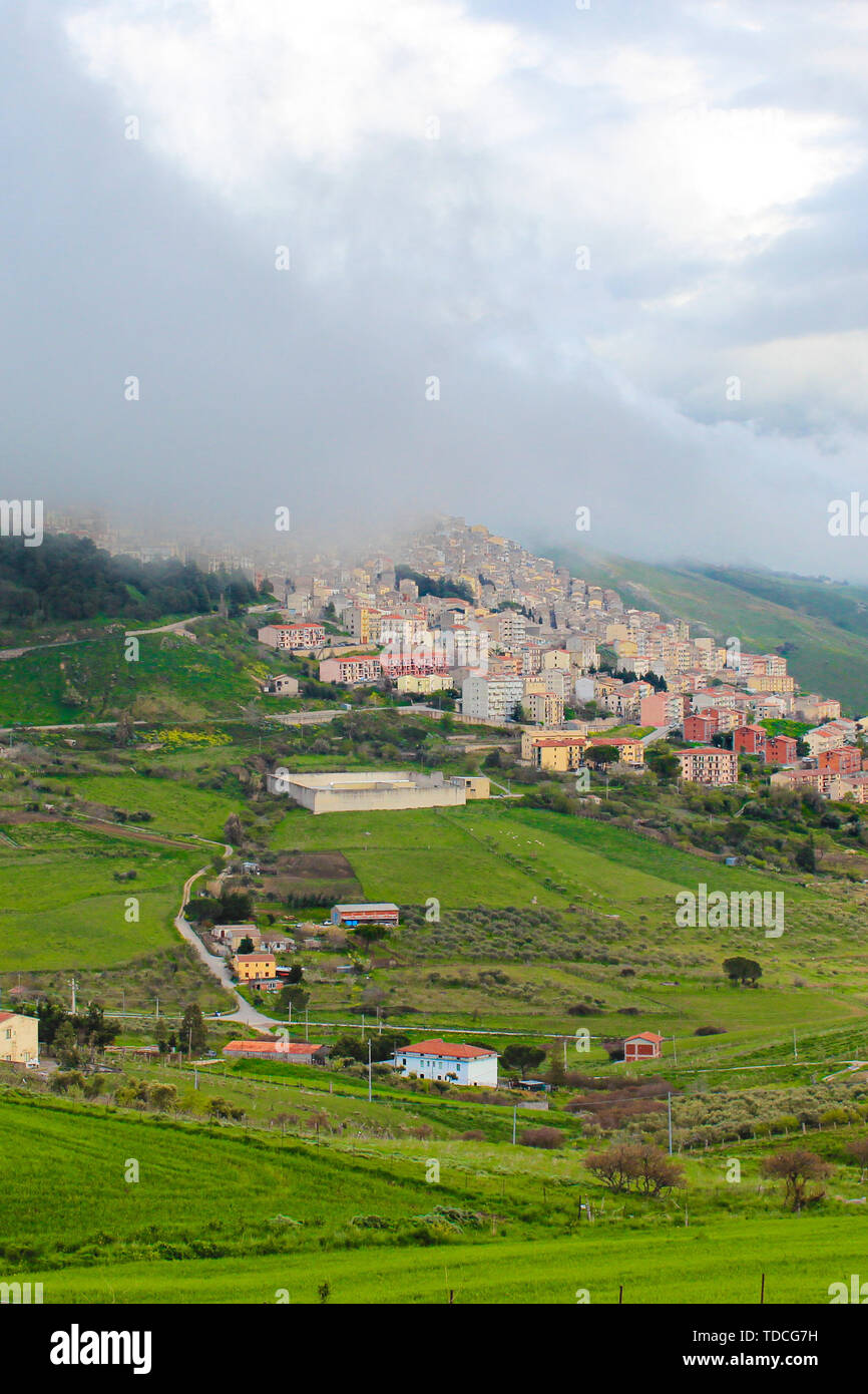 Vertical photo of picturesque Sicilian village Gangi in Italy captured in fog. The small historical city is surrounded by green landscape and is located on the top of the hills. Italian countryside. Stock Photo