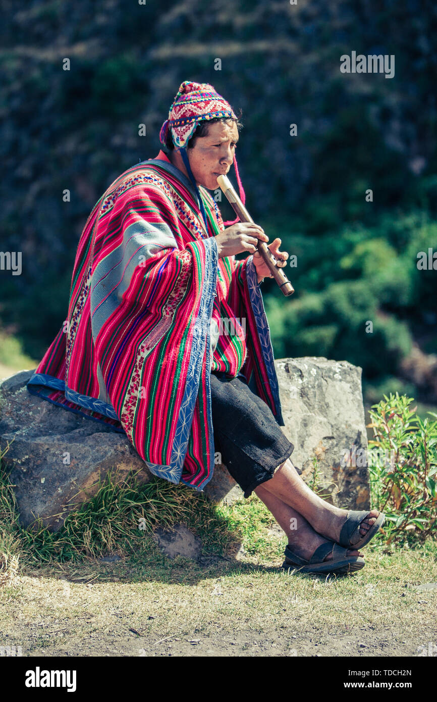 Cusco / Peru - May 29.2008: Portrait of a man, shepherd, goat herder, dressed up in native,costume seating on the rock and playing on the flute. Stock Photo