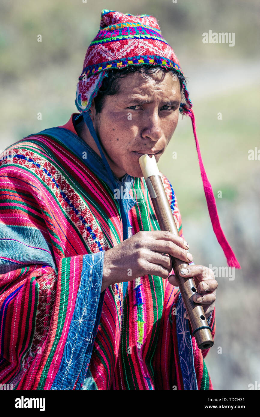Cusco / Peru - May 29.2008: Portrait of a man, shepherd, goat herder, dressed up in native,costume seating on the rock and playing on the flute. Stock Photo