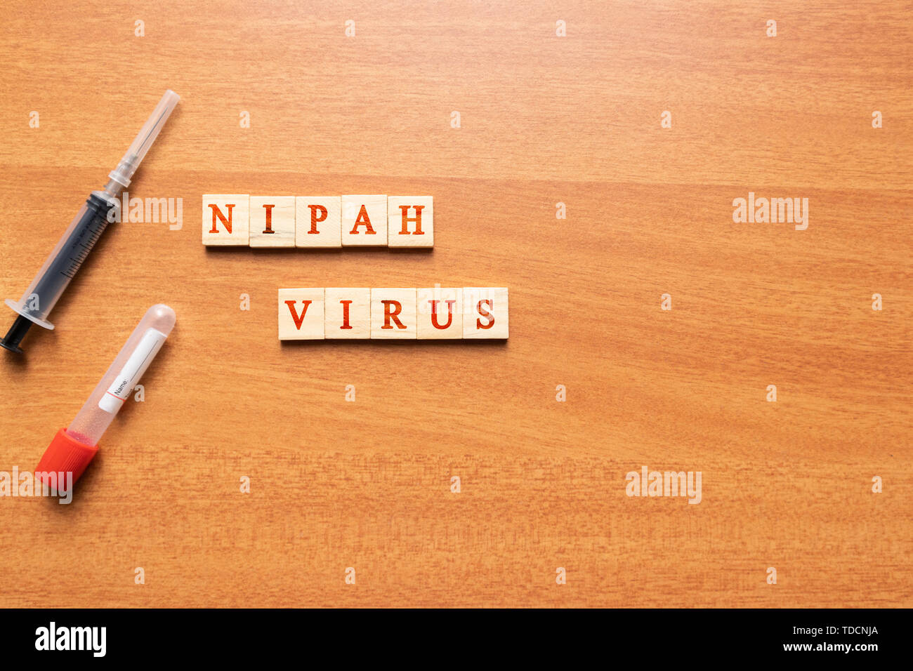 Nipah Virus on a wooden textured background with syringe and vacutainer blood collection tube. Stock Photo