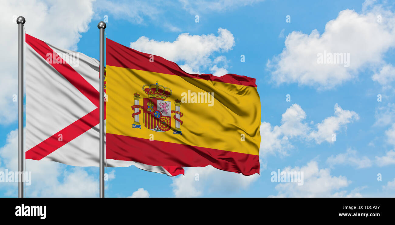 Jersey and Spain flag waving in the wind against white cloudy blue sky ...