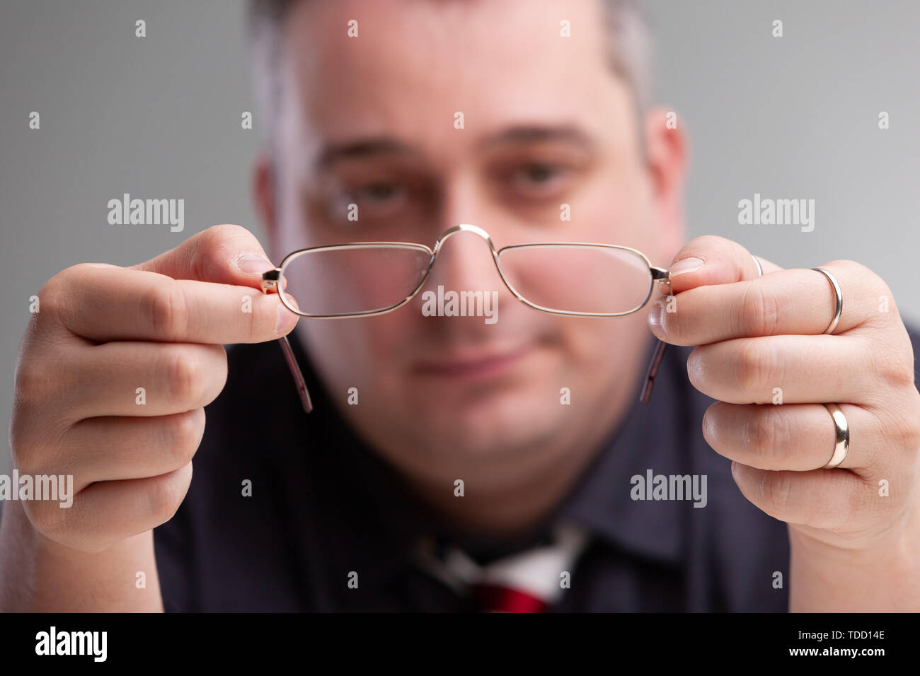 Businessman holding a pair of eyeglasses with metal frames in his hands with a thoughtful expression, selective focus to the spectacles Stock Photo