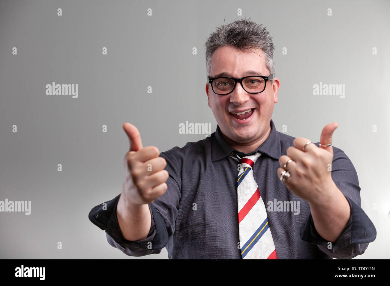 Exultant businessman giving a double thumbs up with a happy gleeful smile as he celebrates a win or victory or offers his support Stock Photo
