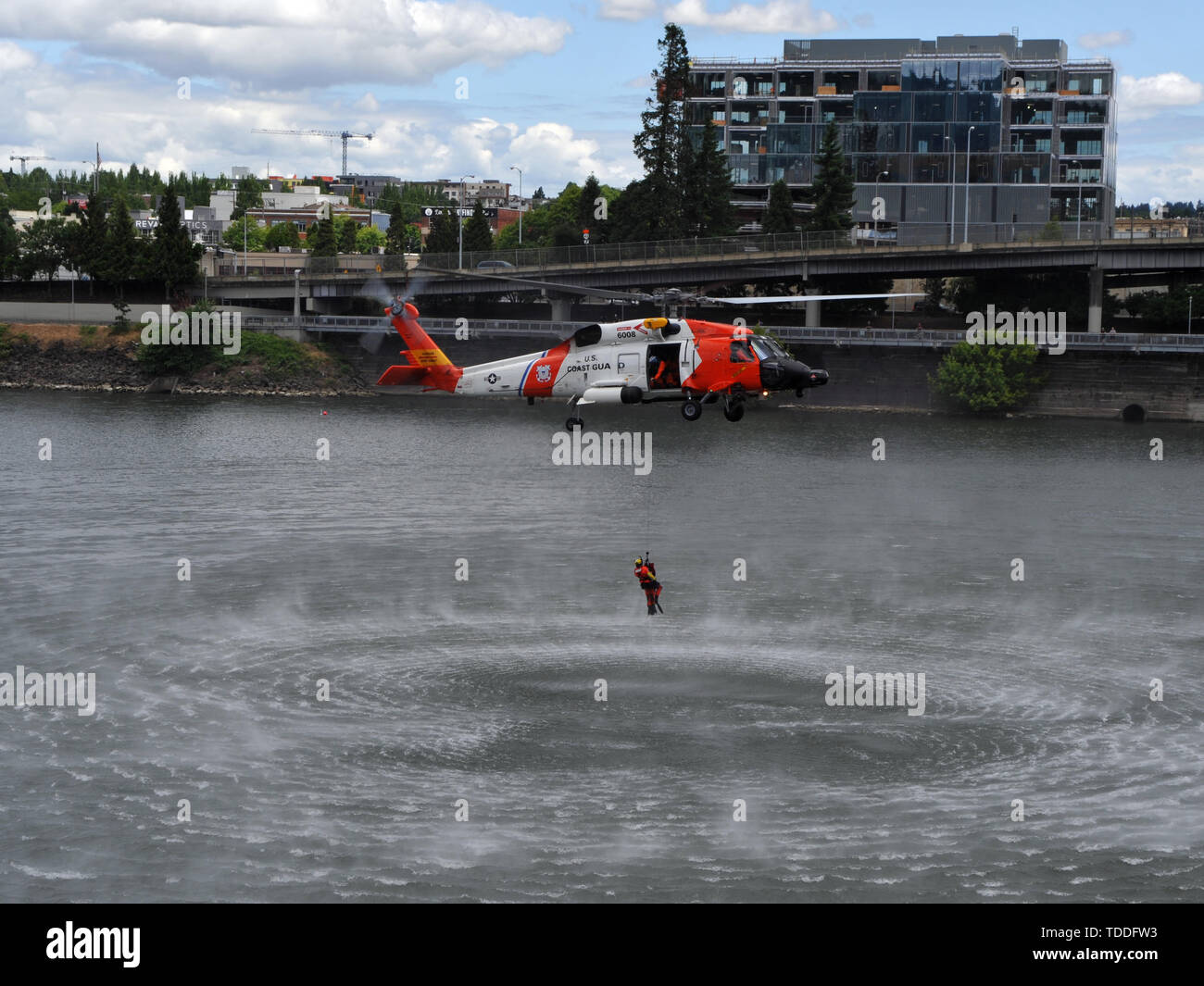 A Coast Guard aircrew aboard an MH-60 Jayhawk helicopter from Sector Columbia River lowers an aviation survival technician into the Willamette River during the Rose Festival in Portland, Ore., June 8, 2019.     The aircrew dropped a training dummy into the river to demonstrate a recovery operation for the thousands of onlookers attending the Rose Festival Fleet Week.     U.S. Coast Guard photo by Petty Officer 3rd Class Trevor Lilburn. Stock Photo