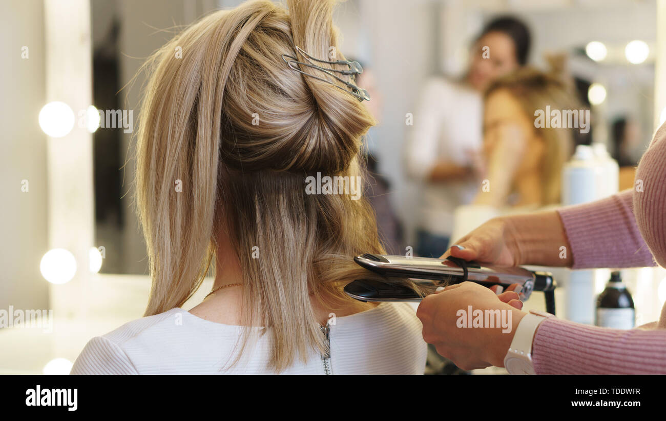 Hairtician twirls curls with flat iron hair. Back view. Hairdressing services. Creation of evening hairstyles fashionable stylish women s hairstyles Stock Photo Alamy
