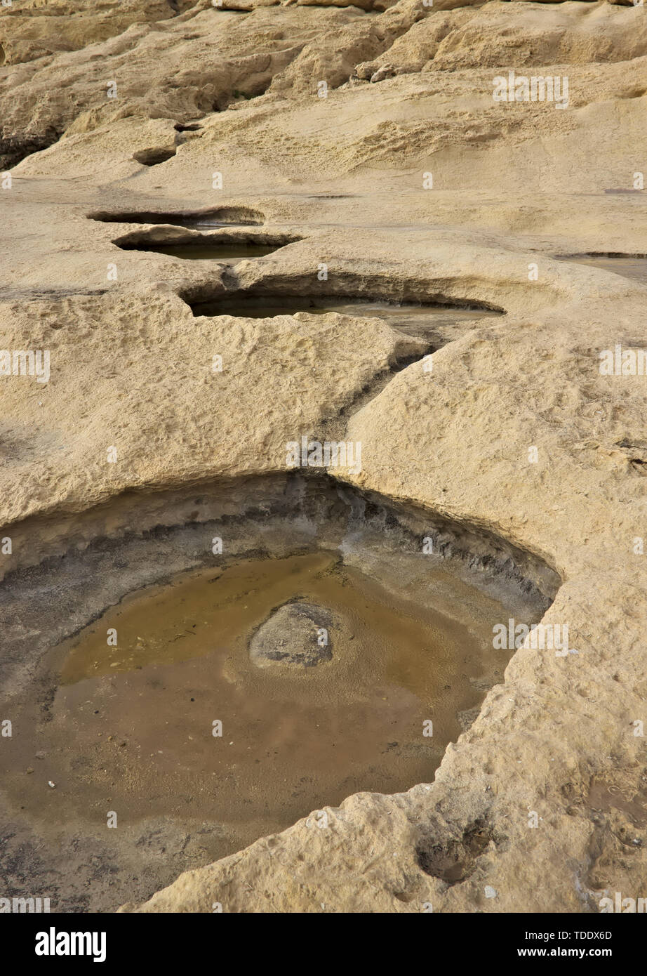 Little holes or pools of water formed in beige limestone at coast in Gozo, Malta. Stock Photo