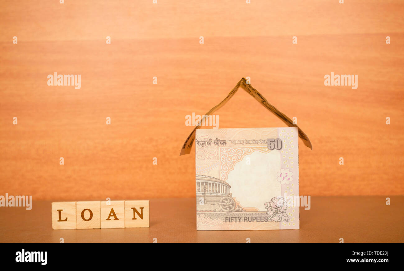 House made from the Indian currency notes and Home Loan in wooden block letters on wooden background. Stock Photo