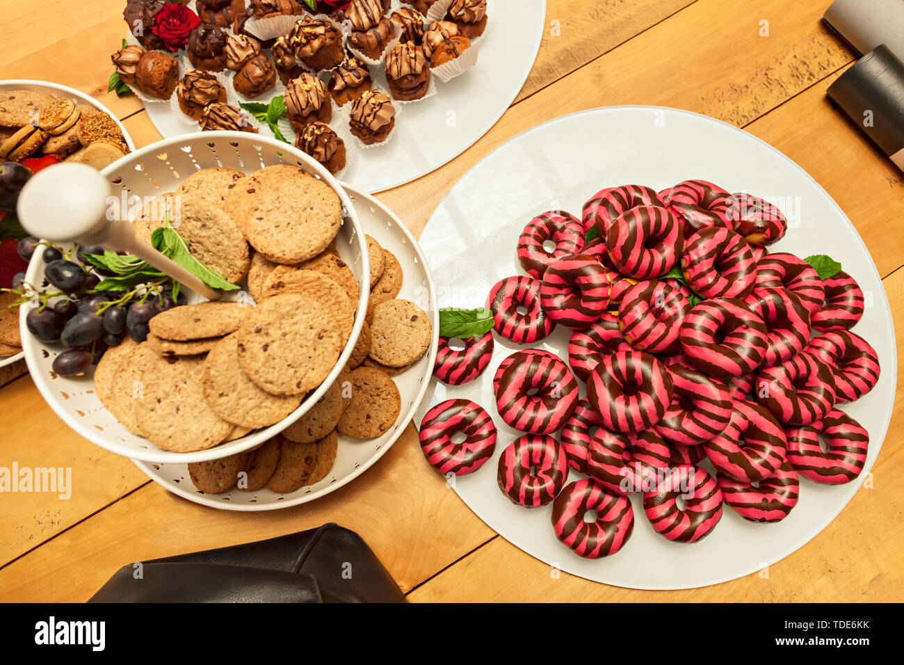 Colorful donuts and variety of sweets laid on a wooden table along with two paper tubes and a black leather bag Stock Photo