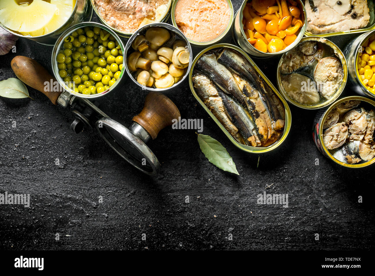 Various canned food in open cans. On black rustic background Stock