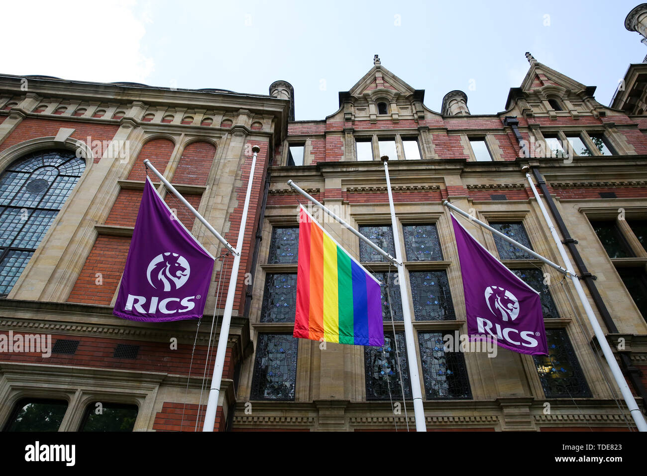 A Pride flag hangs in between RICS flags outside Royal Institution of Chartered Surveyors (RICS ) building in central London in celebration of Pride in London next month. Stock Photo