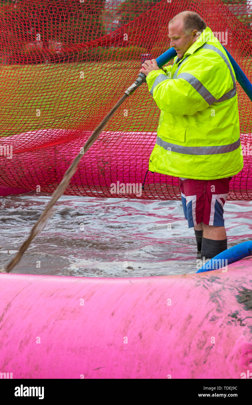 Baiter Park, Poole, Dorset, UK. 15th June 2019. Cold wet day for Race for Life Pretty Muddy. Preparing the mud pool to ensure participants get covered in mud glorious mud! Filling with hose. Credit: Carolyn Jenkins/Alamy Live News Stock Photo