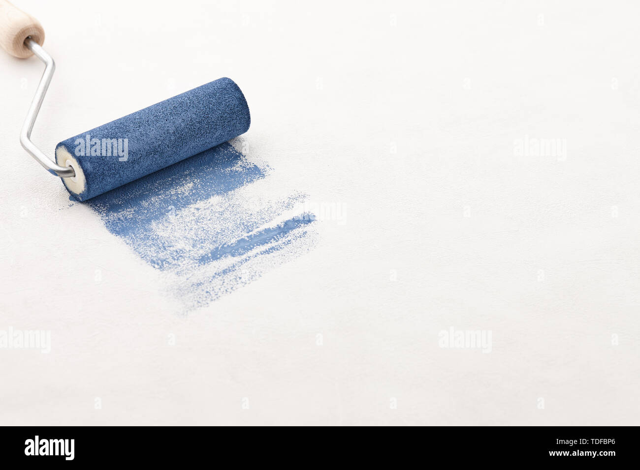 Sponge roller with blue paint on white wallpaper background, copy space Stock Photo