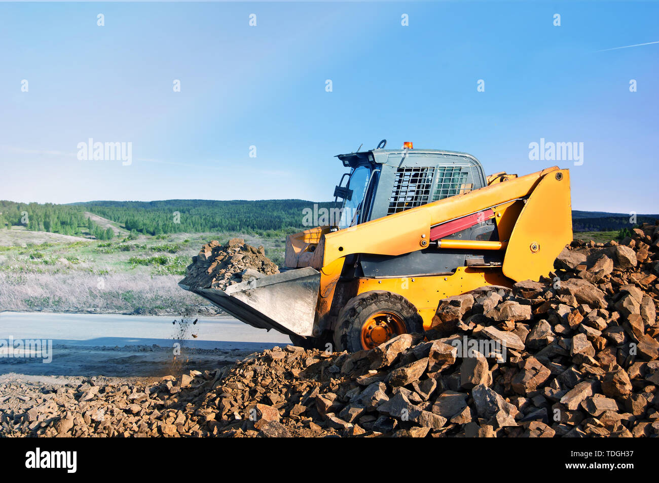 Loader dumping stone on road on the natural background In the countryside. Stock Photo