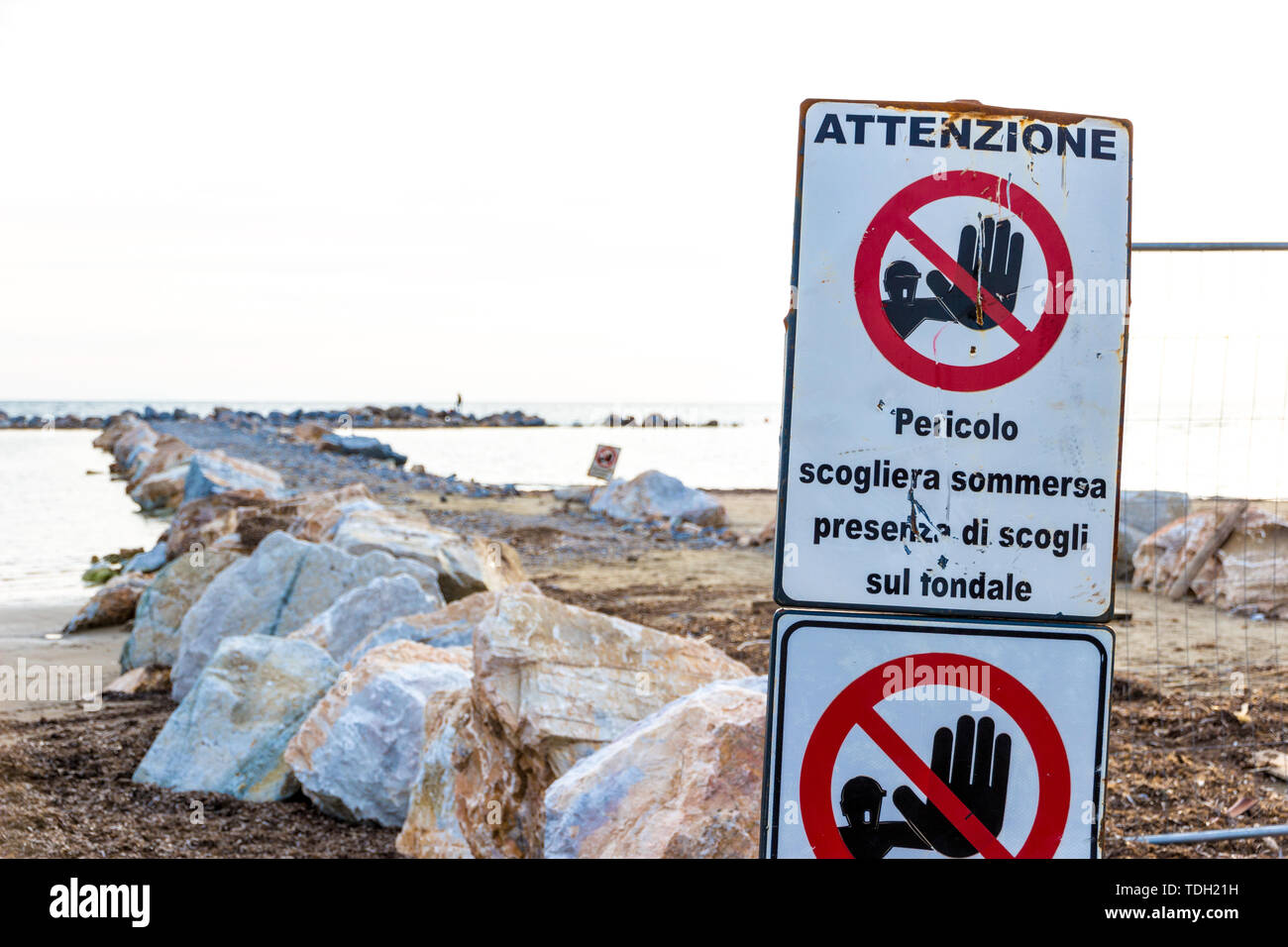 Warning signs reading: 'Warning. Danger submerged reef, rocks on the shoal are present' near a construction site on the shoreline in Follonica, Italy Stock Photo