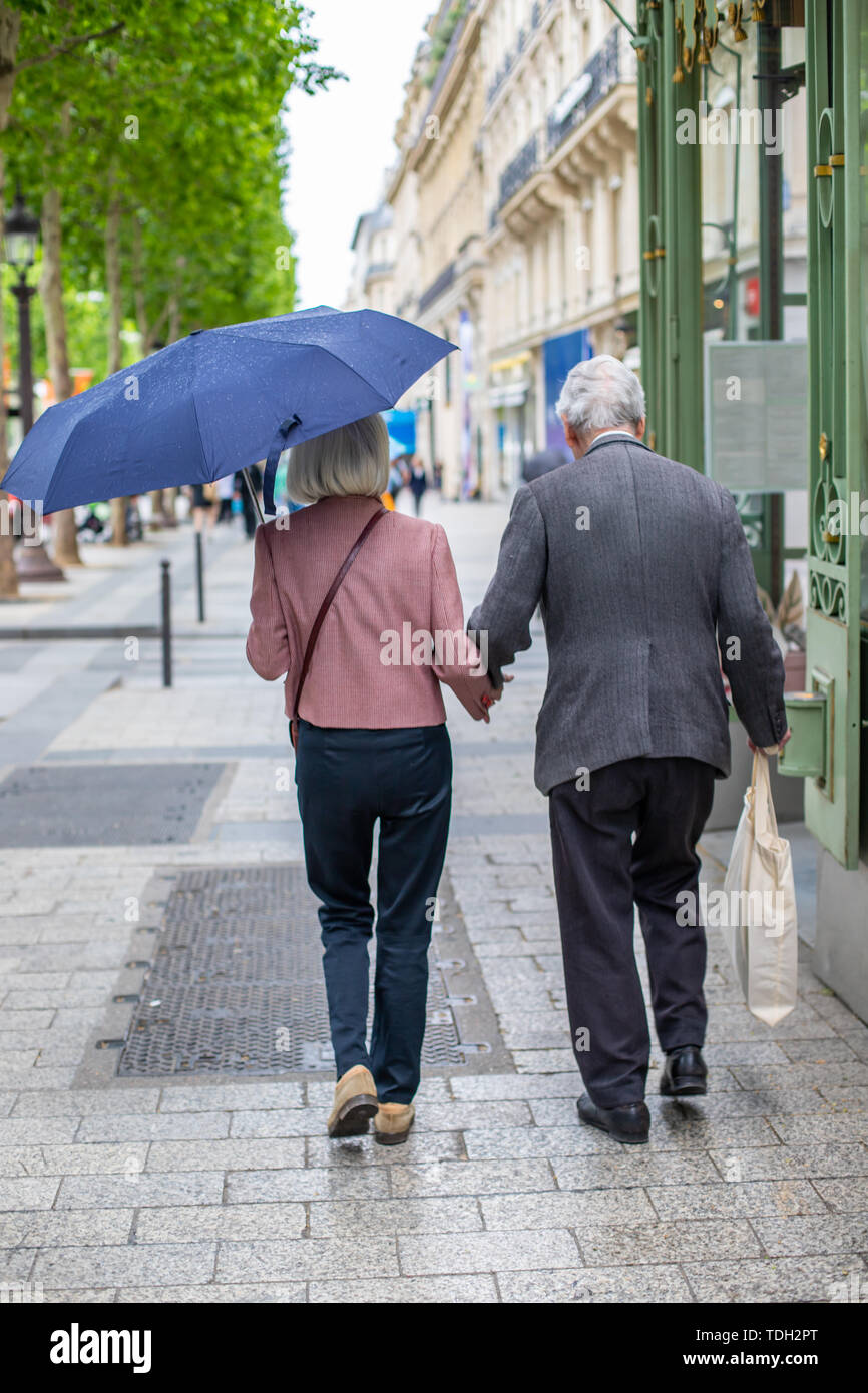 Elderly couple under umbrella holding hands. Loving each other old people go down the street. Stock Photo