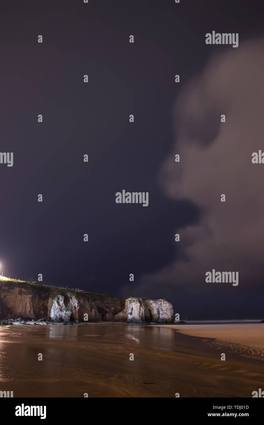 Pareidolia Cloud formation in the shape of a face overlooking cliffs on a beach on in Cornwall on a dark stormy night Stock Photo