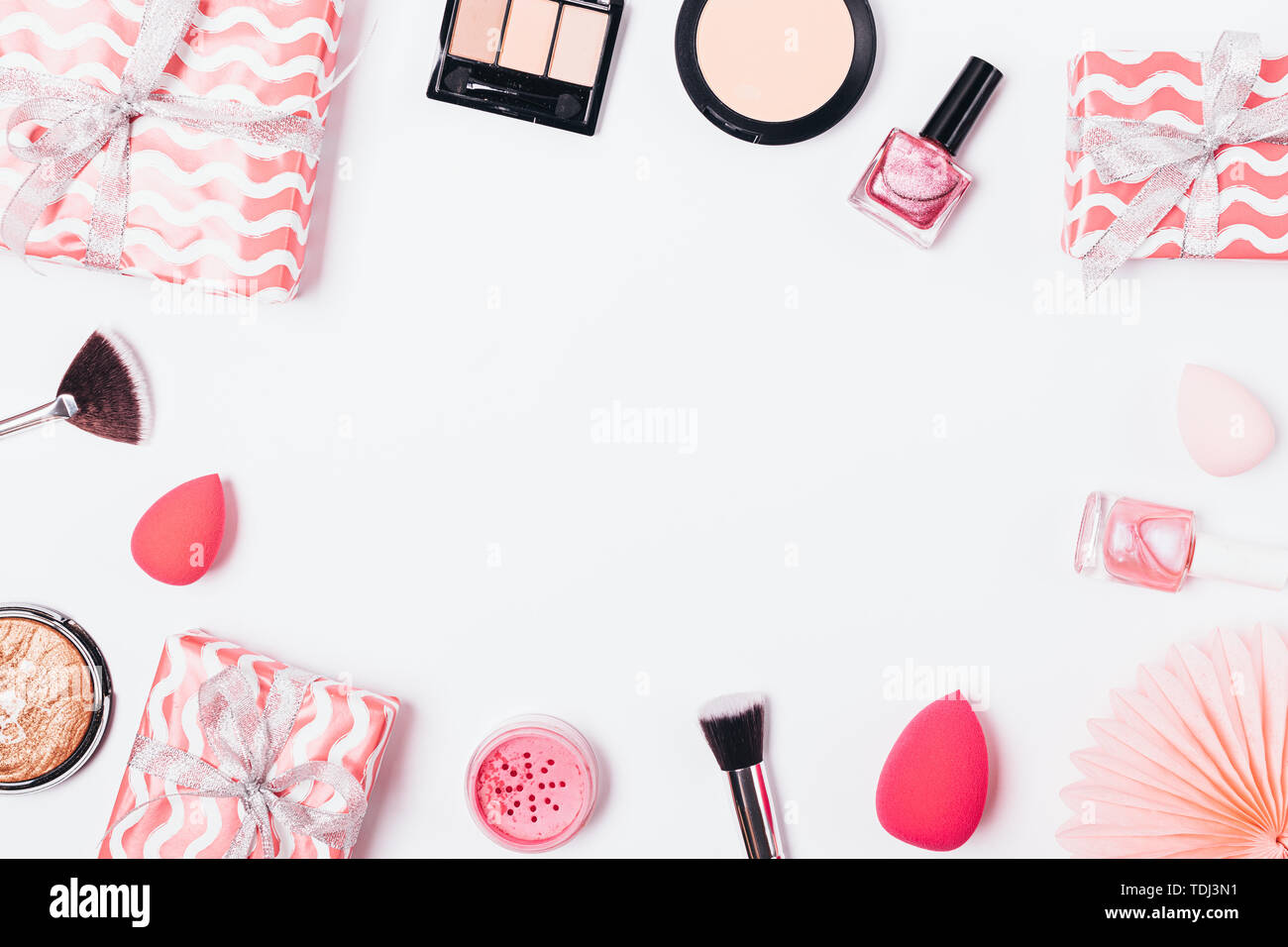 Festive flat lay frame of makeup products and pink gift boxes on white background, overhead view. Stock Photo