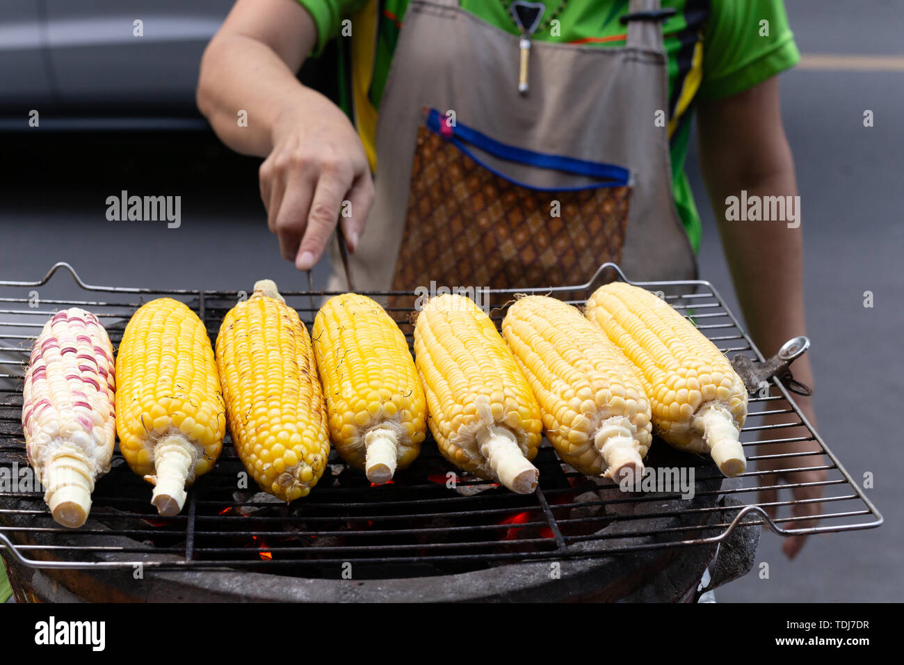 Street food woman grill corn on the cob on the hot stove with charcoal