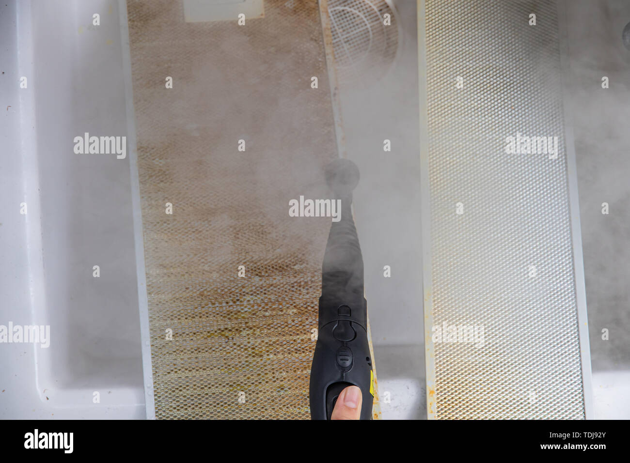 A woman cleaning aluminum filter for kitchen hood by stream machine. Stock Photo