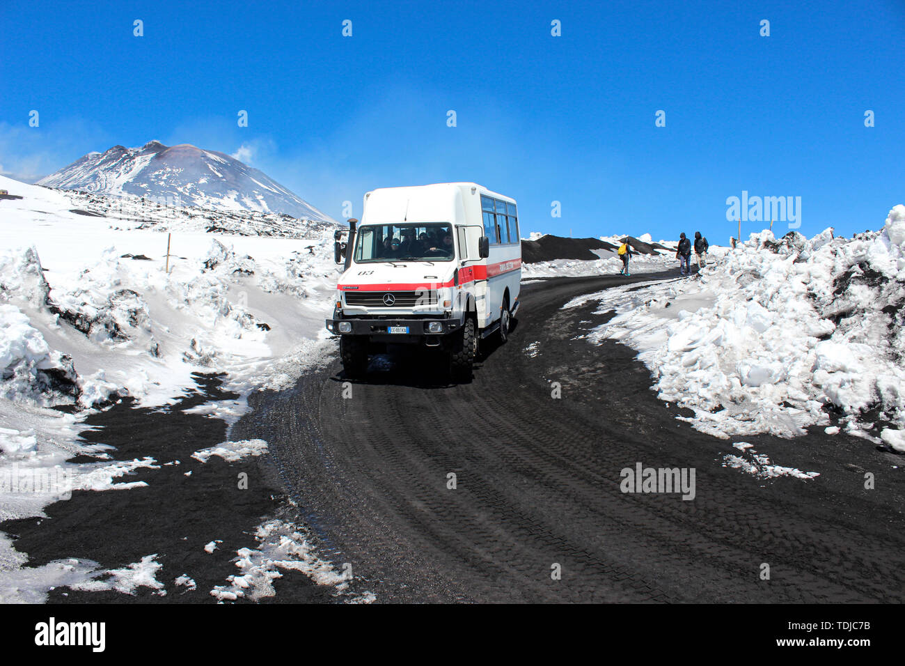 Etna, Sicily, Italy - Apr 9th 2019: Tourist jeep or bus driving tourists to the top of Etna volcano and back. Snow on the volcanic soil along the road. Very top in the background. Stock Photo