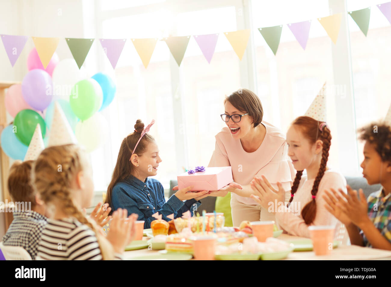 Portrait of excited little girl  receiving gifts during Birthday party with friends, copy space Stock Photo