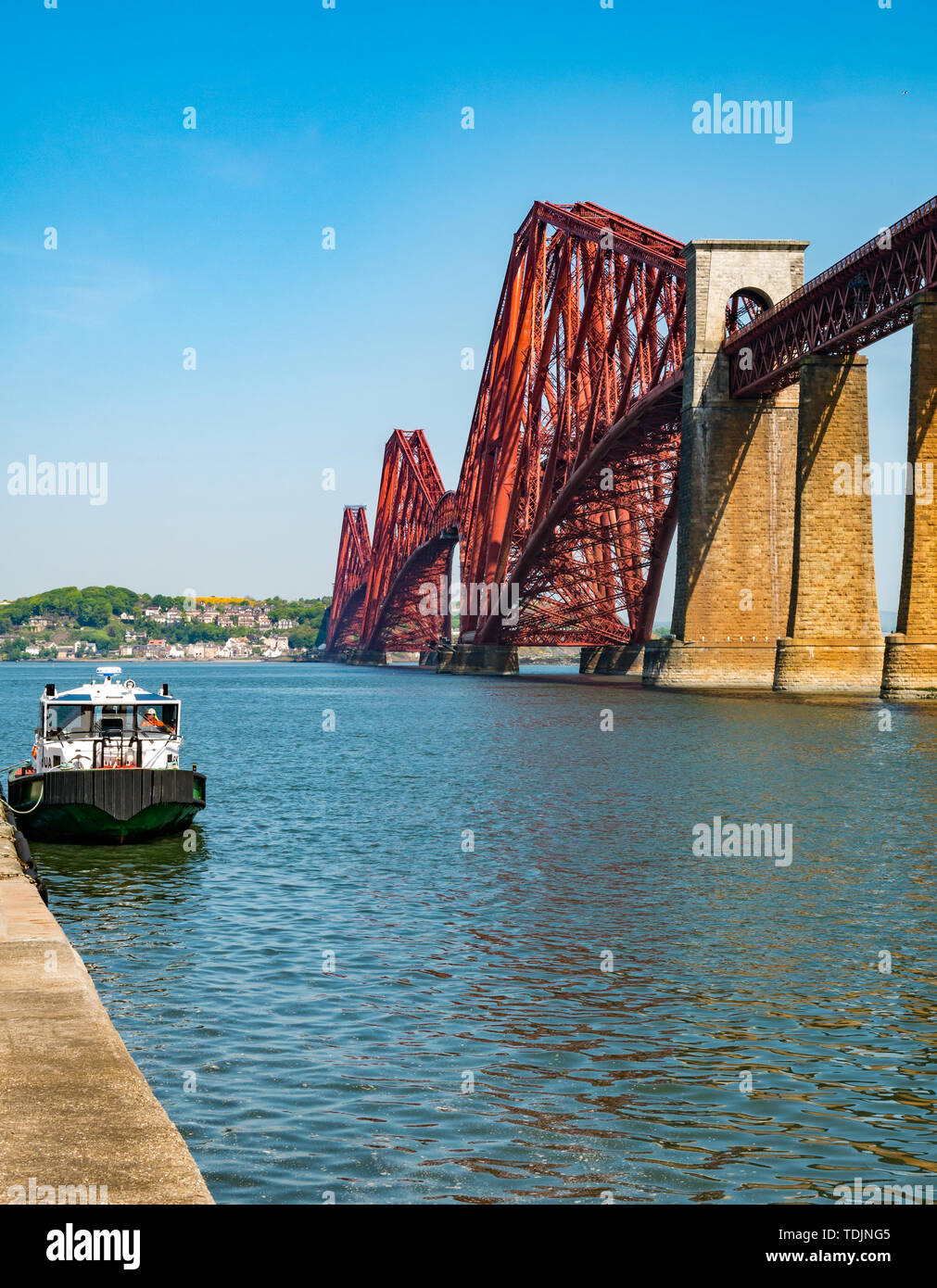Iconic Forth Rail Bridge over Firth of Forth on sunny day with boat at pier, Scotland, UK Stock Photo