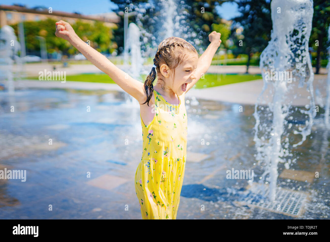 Girl in yellow dress playing and having fun enjoying the spray of the