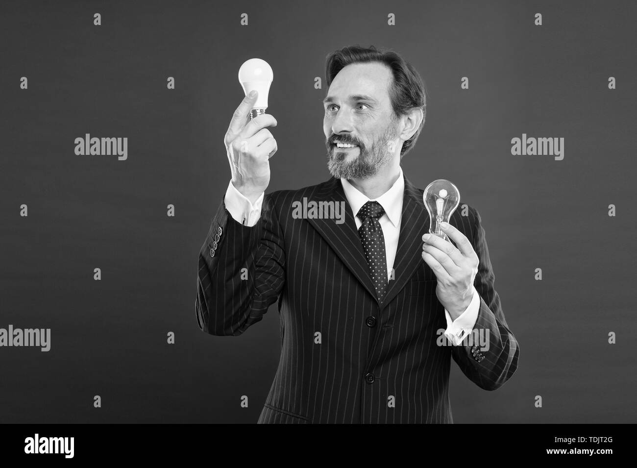 Idea for business. Environment friendly idea. Genius idea. Light up your business. Man bearded businessman formal suit hold light bulb on red background. Symbol of idea progress and innovation. Stock Photo