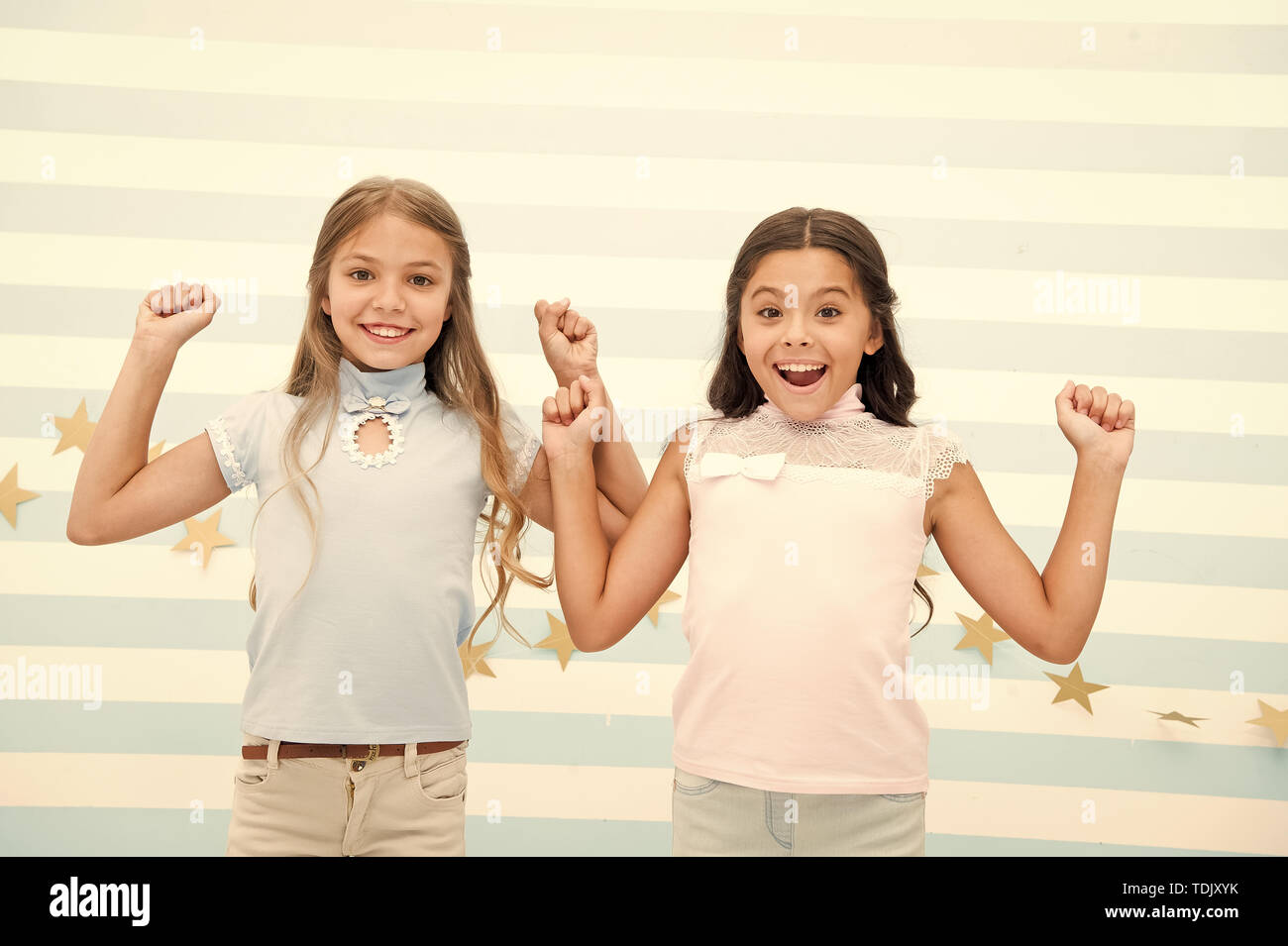 Thrilled moments together. Kids schoolgirls preteens happy together. Girls smiling happy faces excited expression stand striped background. Girls children best friends thrilled about surprising news. Stock Photo