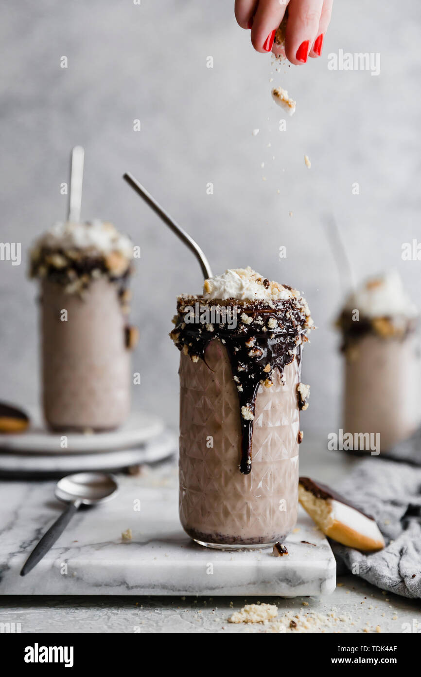 Black and white milkshake. A hand sprinkles a topping on a milkshake