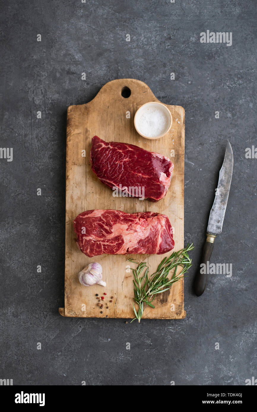 Raw black angus prime beef steak variety on vintage cutting board with rosemary, sea salt and spices Stock Photo