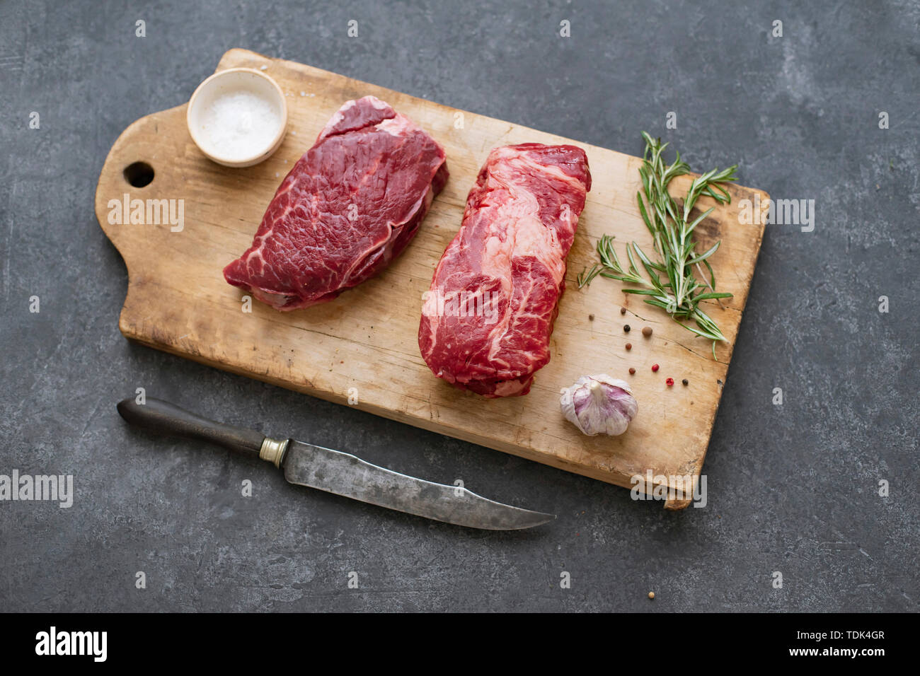 Raw black angus prime beef steak variety on vintage cutting board with rosemary, sea salt and spices Stock Photo