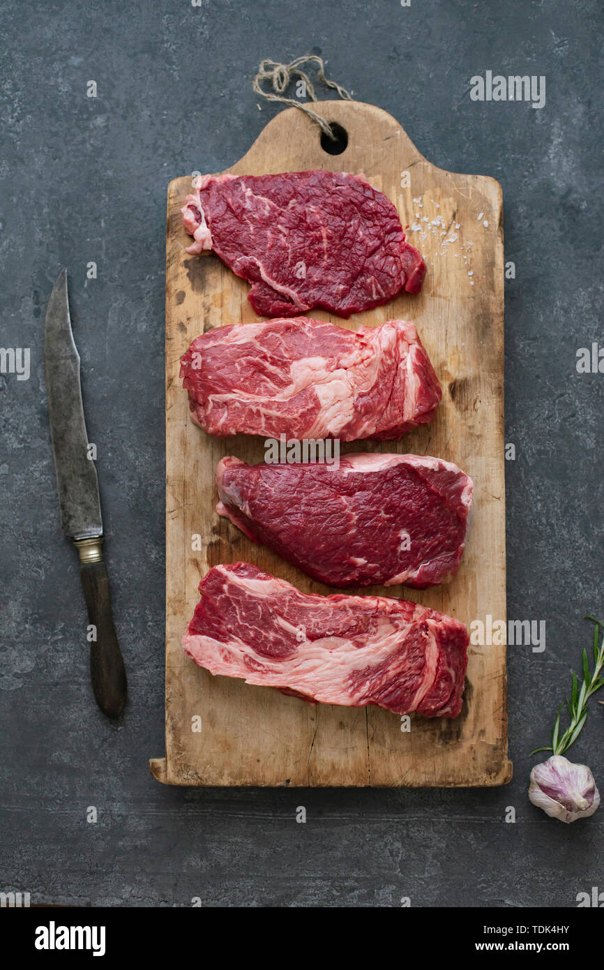 Raw black angus prime beef steak variety on vintage cutting board with rosemary, sea salt and spices Stock Photo