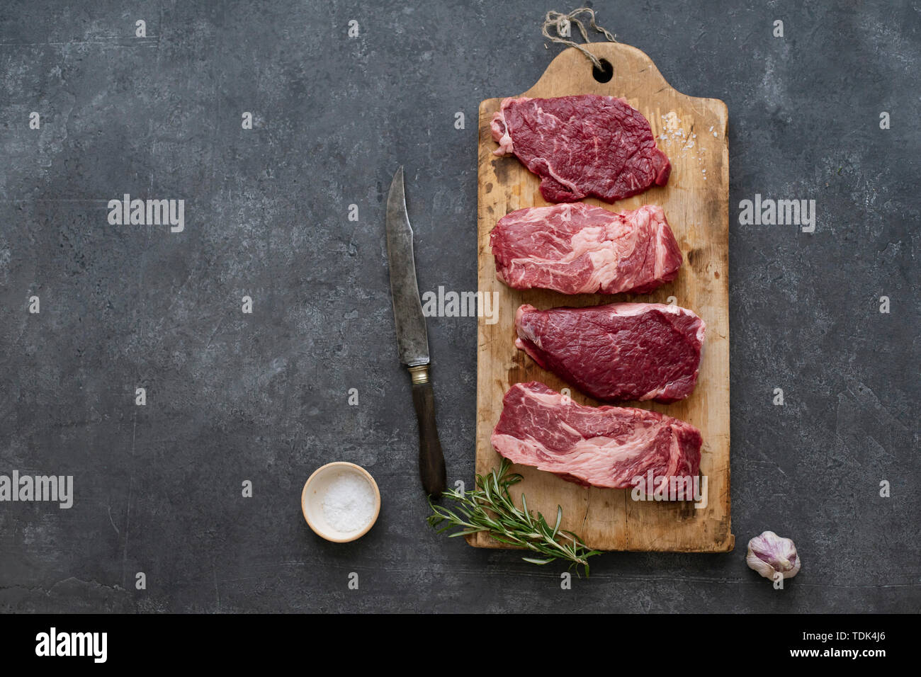 Raw black angus prime beef steak variety on vintage cutting board with rosemary, sea salt and spices Stock Photo