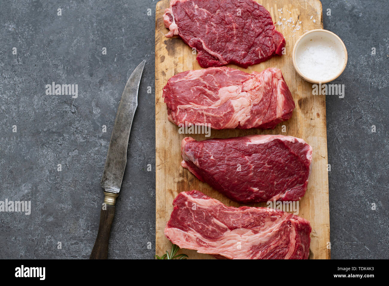 Raw black angus prime beef steak variety on vintage cutting board with rosemary, sea salt and spices Stock Photo