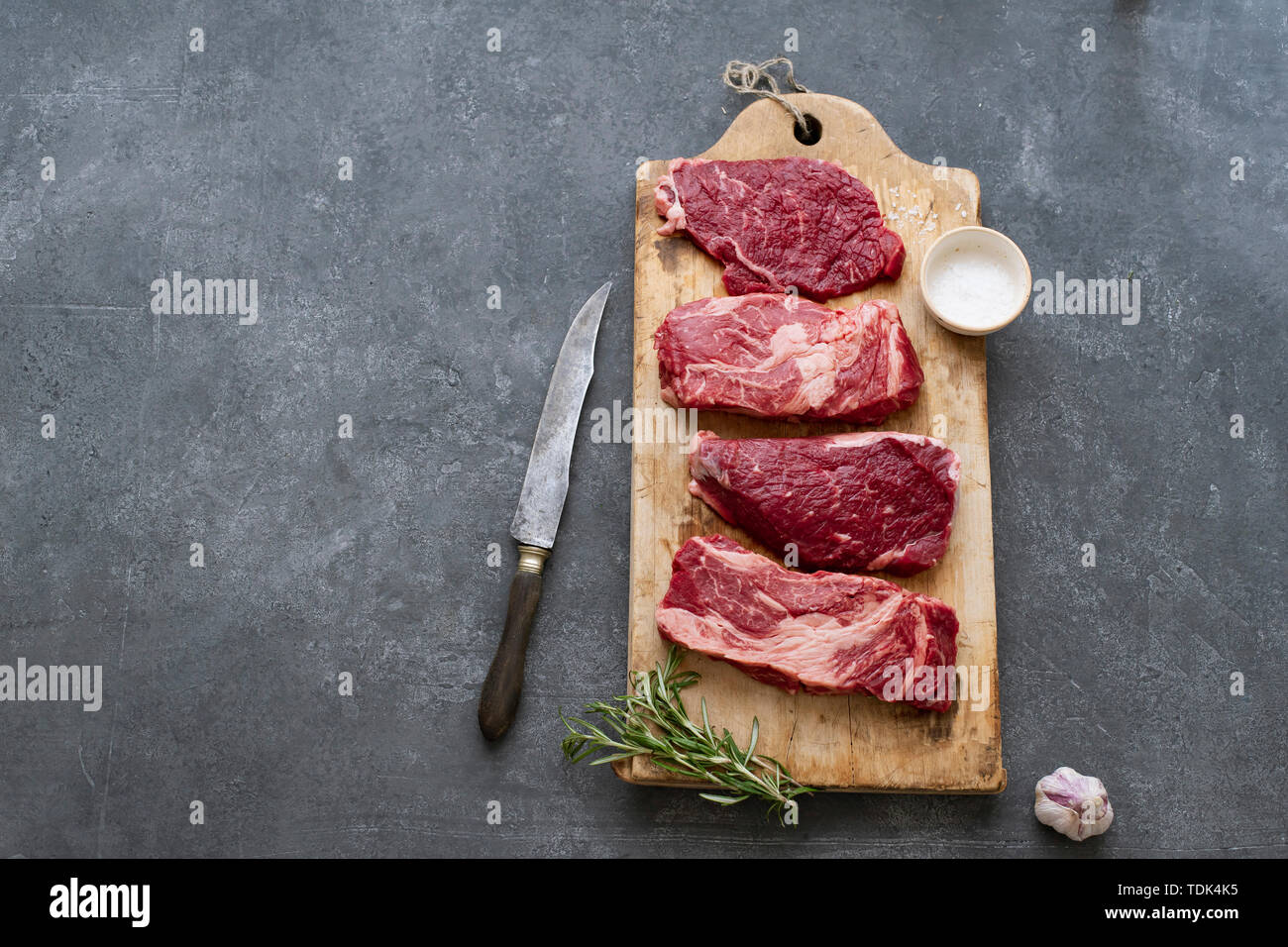 Raw black angus prime beef steak variety on vintage cutting board with rosemary, sea salt and spices Stock Photo